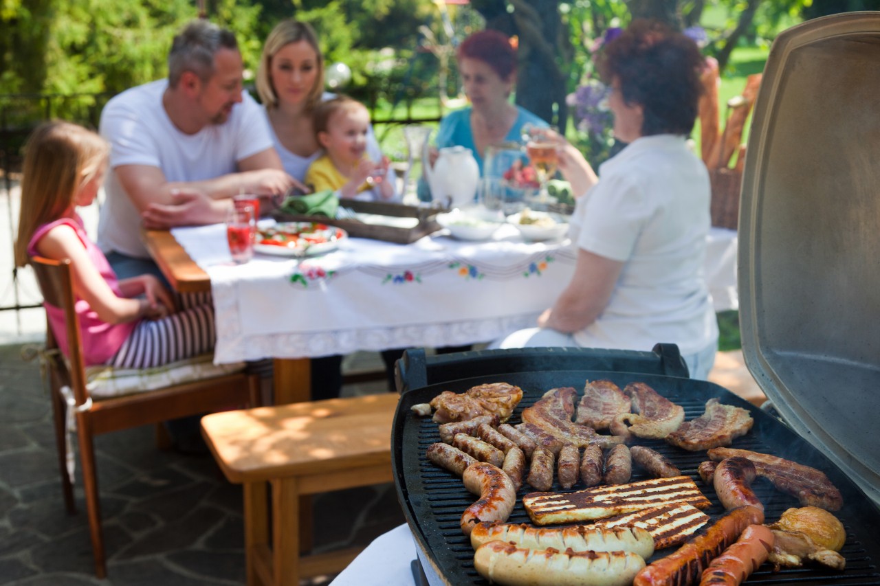 Meat on grill with family at dinner table in background